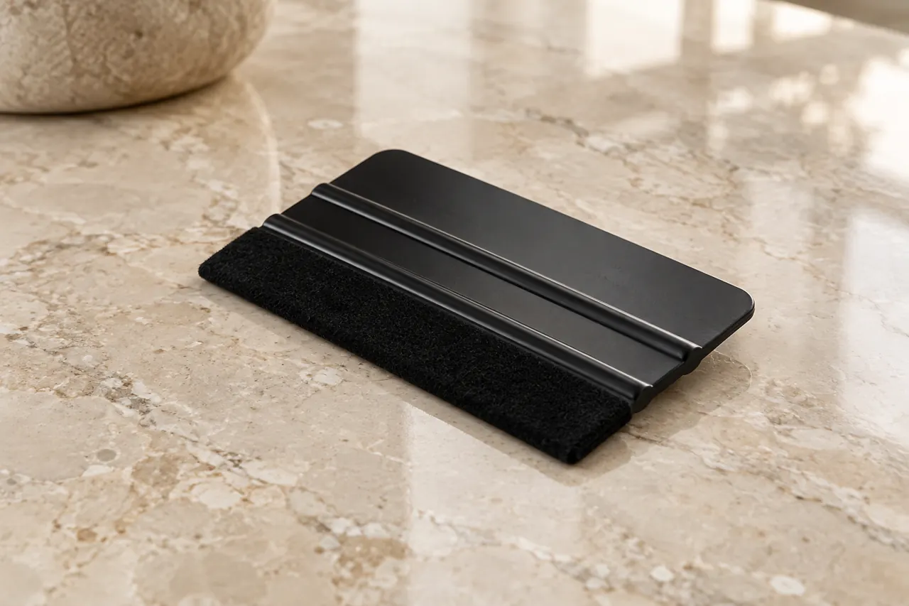 One premium black felt-edged application squeegee resting on a lightly reflective cream stone worktop, studio product photograph