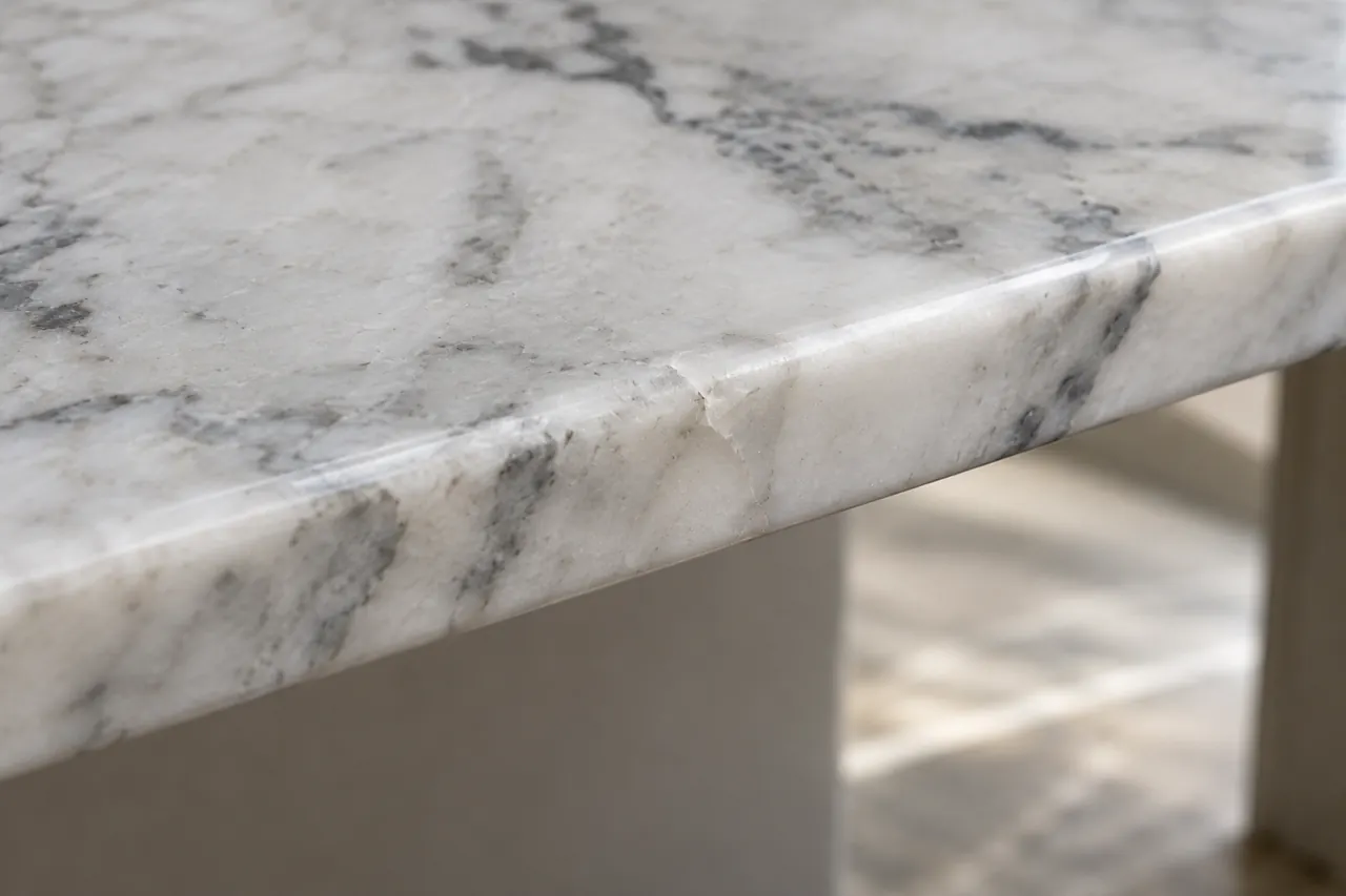 Close detail of a small carefully filled repair in a white marble edge with natural grey veins, the repair subtly visible, realistic modest finish